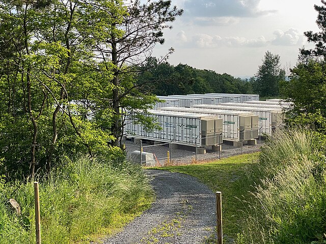 Battery energy storage systems situated in a clearing of a wooded area with green trees and a small pathway.
