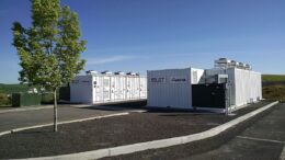 Battery energy storage system with containers and a tree and sky in the background.